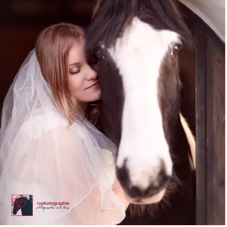 Frau im Hochzeitskleid schmust liebevoll mit ihrem Pony